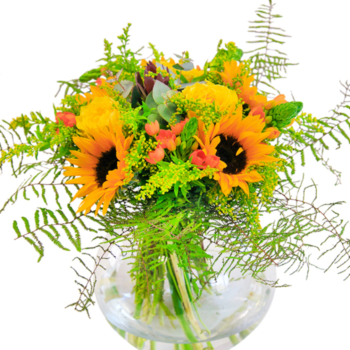 The essence of sunlit celebration is captured in this exuberant Harrow Weald bouquet, arranged with care by local floral artisans to mirror the vitality of summer at its peak. Towering sunflowers, with their signature chocolate-brown centres and lively petals in yellows and orange, bring a sense of radiance and joy-much like the community spirit often found in the heart of Harrow Weald. Alongside, impeccably formed yellow garden roses spread their layers wide, spiralling outward as if sharing their warmth with every glance. Between these showstoppers, clusters of vibrant red Hypericum berries glisten, their vivid tones providing a festive accent that dances amidst deep green and bluish eucalyptus foliage. Delicate ferns spill over the glass vase's round rim, lending softness and a sense of motion, reminiscent of leafy shadows dappling the grounds near Harrow Weald Recreation Ground. Light green filler flowers-possibly goldenrod-speckle the arrangement with tiny yellow blossoms, drawing the eye deeper into the bouquet's intricate composition. The transparent vase allows a close look at the colour-rich stems as they mingle and nestle in fresh, shimmering water. There's a gentle perfume of roses and fresh greenery, evoking walks down The Common on summer mornings. Ideal for commemorating life's happiest occasions-a friend's birthday, a golden anniversary, or welcoming a bright new chapter-this bouquet pays tribute to both natural artistry and the unique beauty of Harrow Weald.