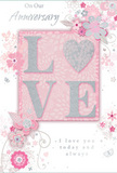 This anniversary card appears as a refined celebration of enduring love, with a colour palette that drifts gently between powder pink, pearl white, and misty silver-tones that would sit beautifully beside a vase of soft roses on a Harrow Weald mantelpiece. At the centre, the word "LOVE" is set in tall, embossed capitals, each letter coated with a fine dusting of glitter so that it catches the light in a way that feels luxurious yet understated. The letterforms rise noticeably from the surface, giving a tactile appeal that would be instantly felt when fingertips brush across the card. Encircling this focal word is a delicate halo of illustrated flowers and swirling vines, their petals shaped in rounded, romantic curves and shaded in gentle blush, lilac-tinged pinks, and pale greys. Flourishes of slender leaves and tiny buds weave through the design, recalling the precise yet flowing style of a florist sketching an anniversary bouquet before arranging fresh stems for local delivery. The background is a soft pink wash, smooth and luminous, which allows the white and silver details to glow without harsh contrast. There are subtle hints of silver foil along edges and centres of some blooms, giving the impression of dew on petals after a cool morning near Harrow Weald Common. Alongside the floral motif, flowing script shares tender anniversary sentiments, the writing spaced thoughtfully so the card never feels crowded. The overall atmosphere is of intimate celebration and heartfelt gratitude-a keepsake that pairs beautifully with a hand-tied bouquet for an anniversary at home in Harrow Weald.